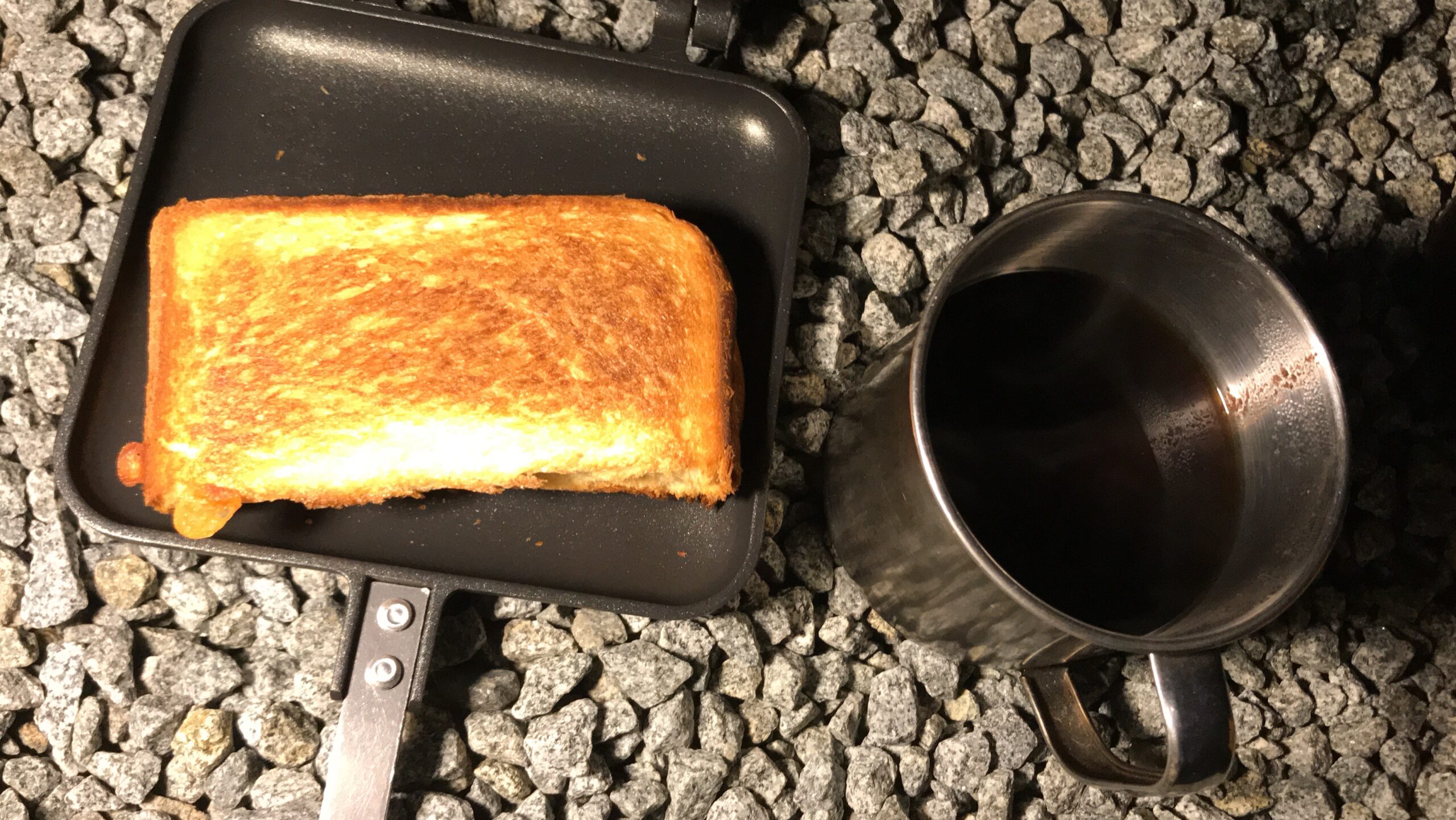 ホットサンドメーカーに載った焼き色のついたパンと金属カップのコーヒー