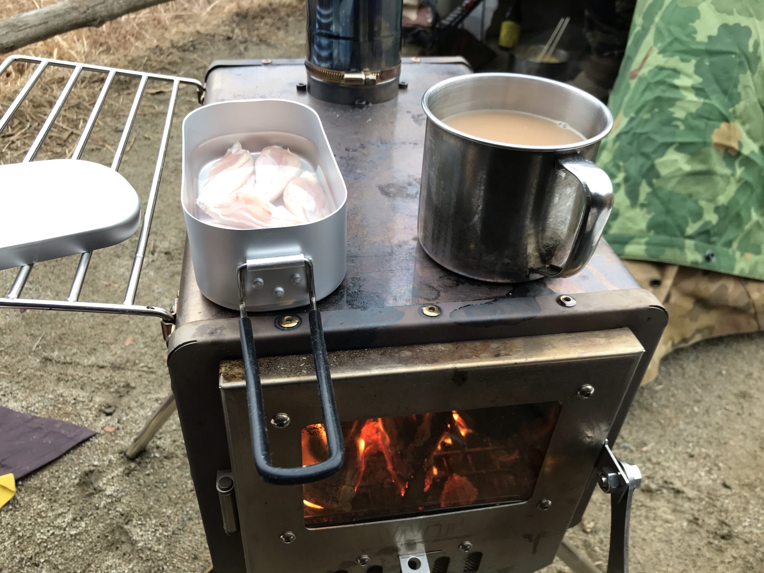 火の入った薪ストーブの天板に置いたメスティンの鶏肉と飲み物