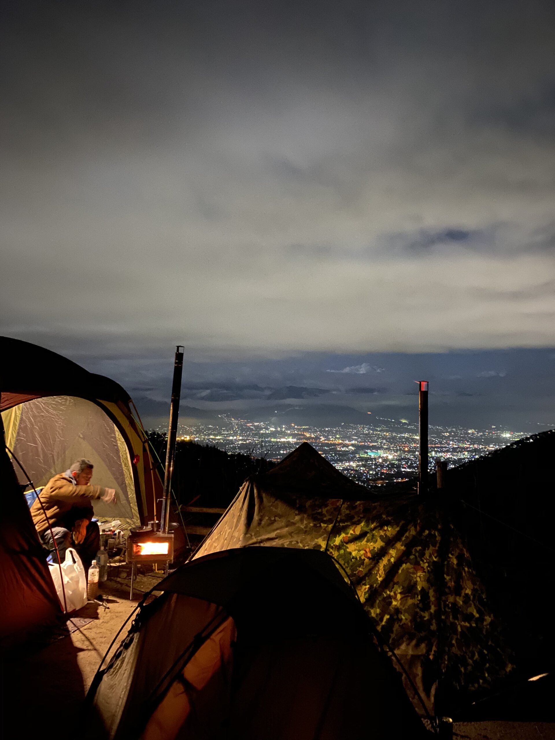 ほったらかしキャンプ場のテントと薪ストーブの向こうに広がる甲府盆地の夜景