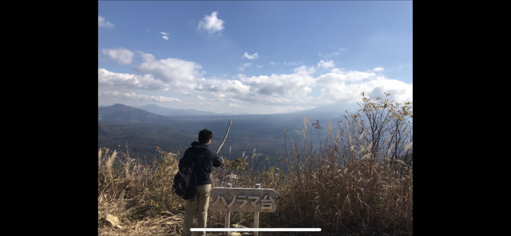 パノラマ台の標識前に立つ登山者と広がる山並み